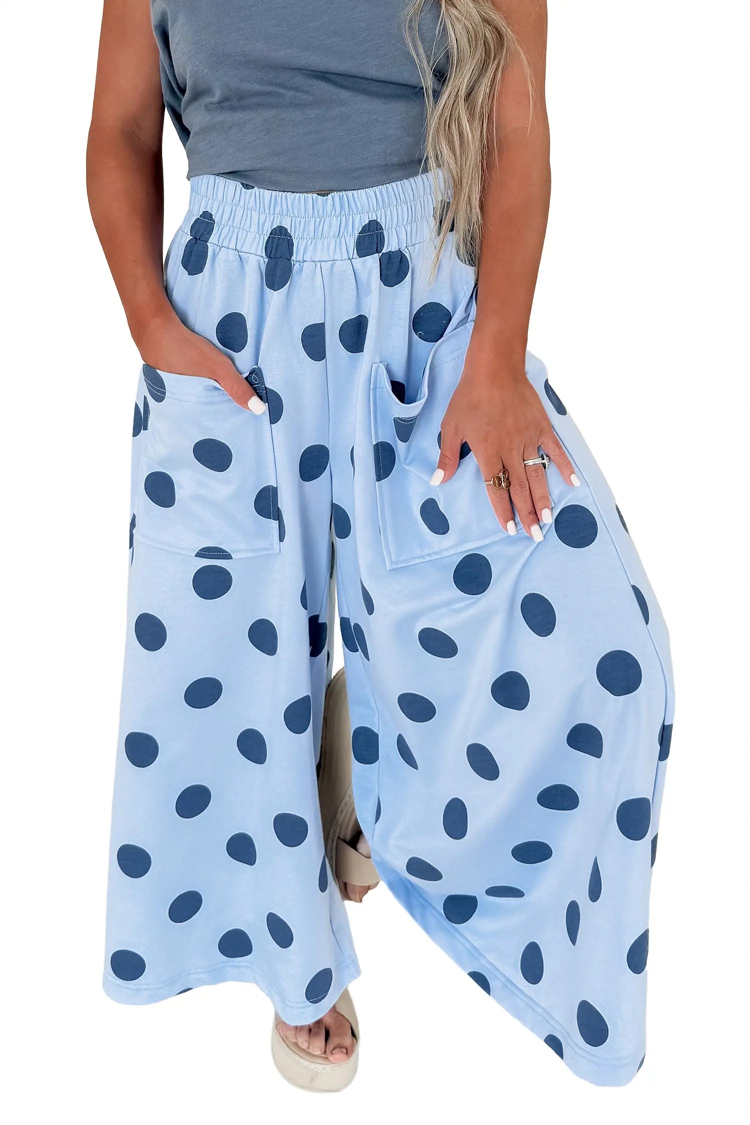 A person wearing light blue wide-leg pants with dark blue polka dots, paired with a gray sleeveless top and beige sandals, shown against a plain white background.