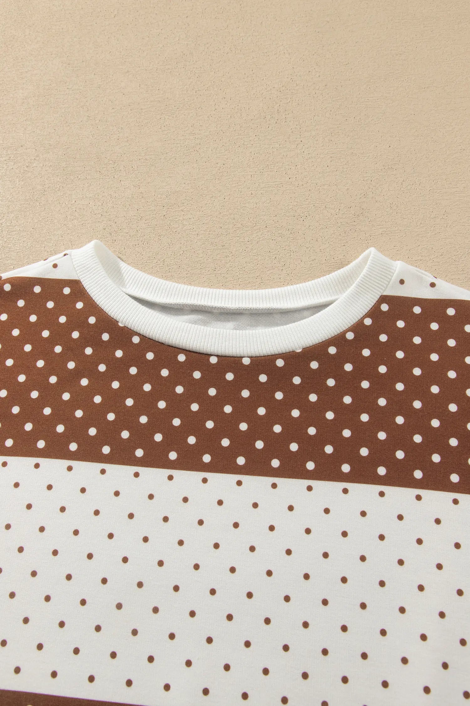 Close-up of a brown and off-white color-blocked top with white polka dots and ribbed neck.