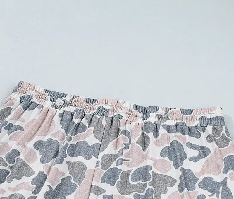 Close-up of a pair of shorts with an elastic waistband, featuring a pink, gray, and white camouflage pattern, set against a plain light gray background.