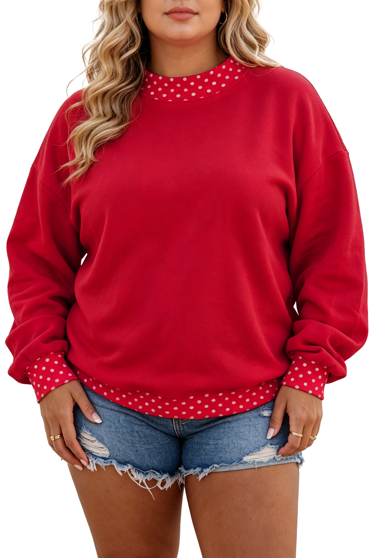 A woman wearing a red crewneck sweatshirt with white polka dot trim on the collar, cuffs, and hem, paired with distressed denim shorts.