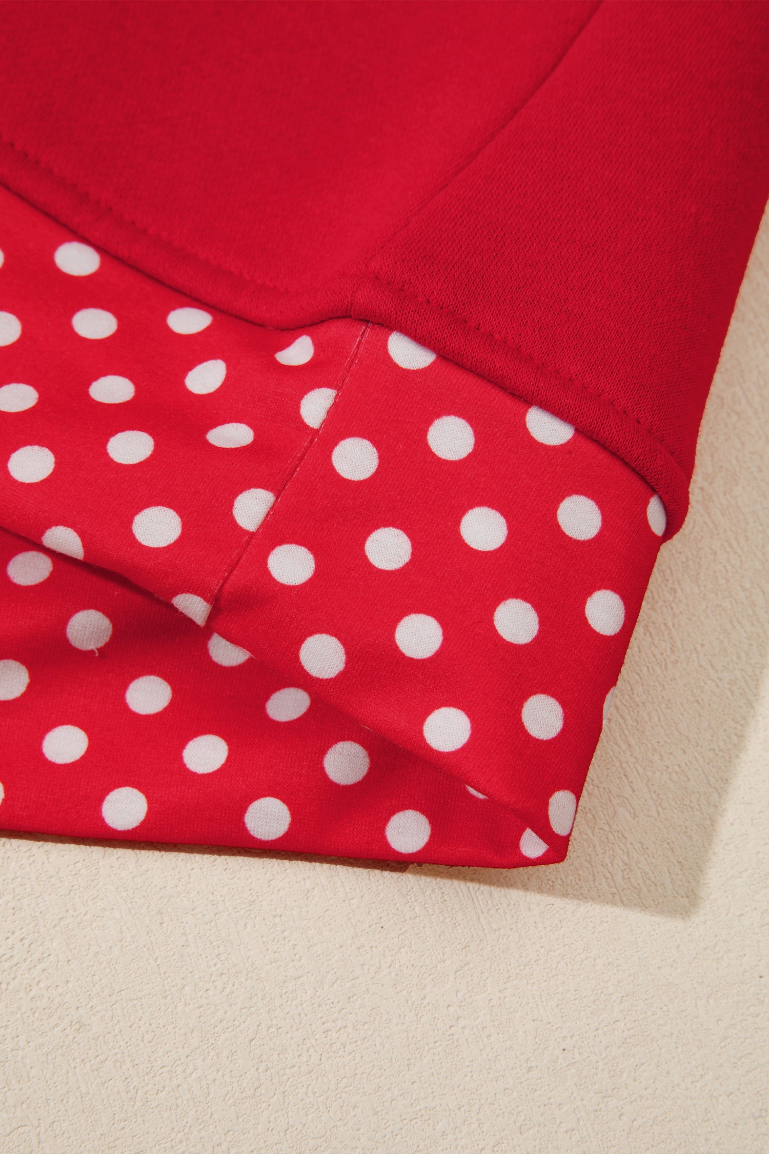Close-up of a red garment with a white polka dot pattern on one folded section and a solid red fabric on another section, laid on a light beige surface.