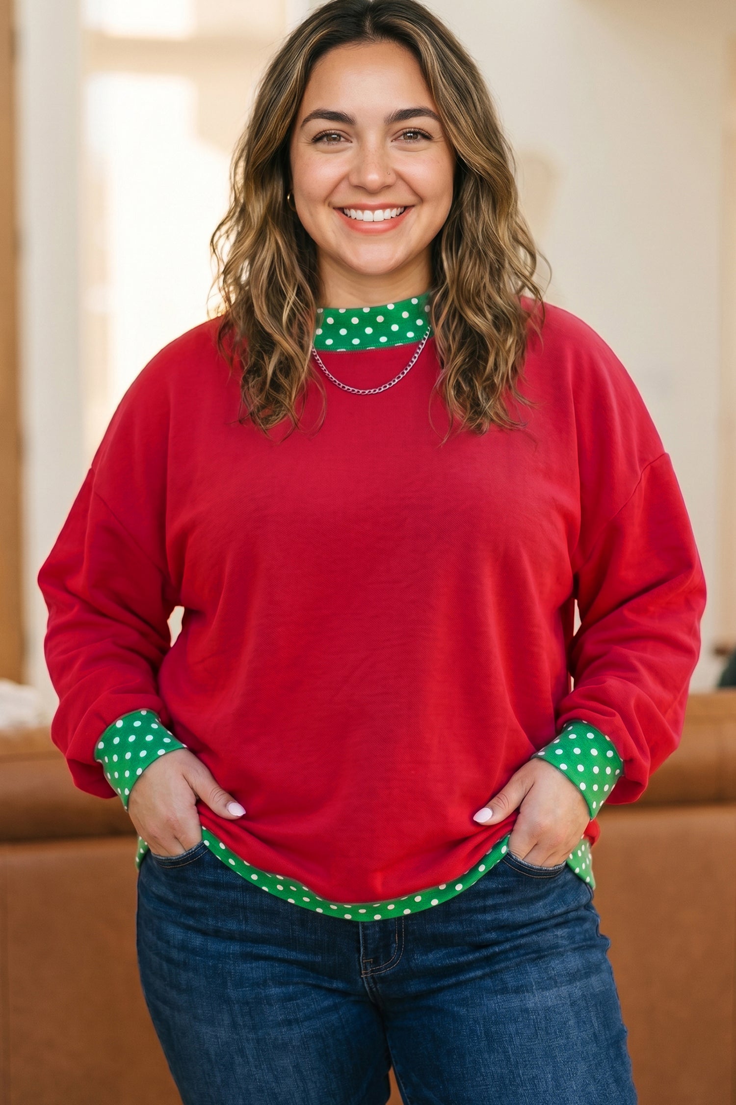 A woman wearing a festive red crewneck sweater with green and white polka dot accents on the collar and cuffs, paired with blue jeans.