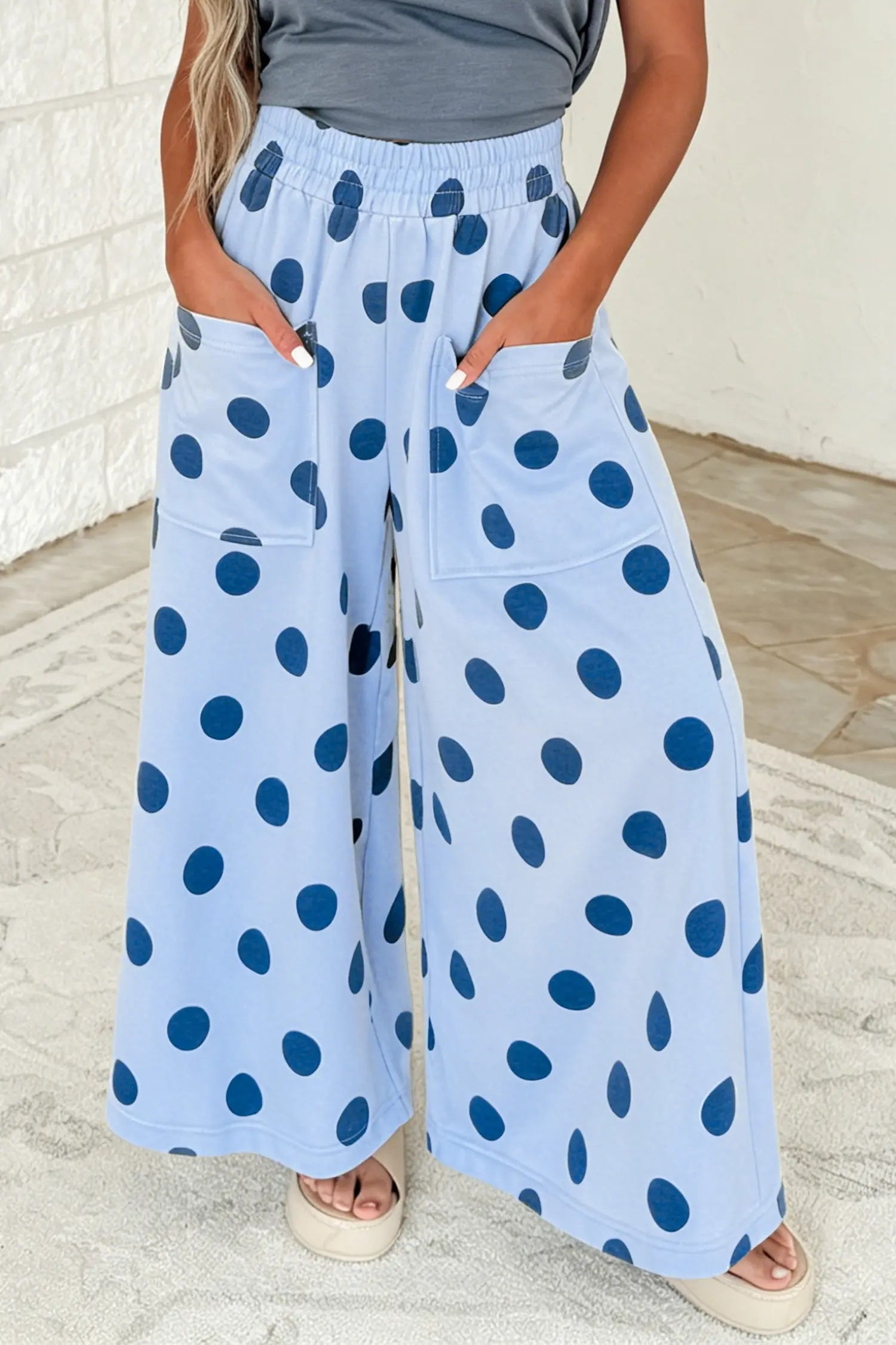 A person wearing light blue wide-leg pants with dark blue polka dots, standing indoors against a white wall and light floor.