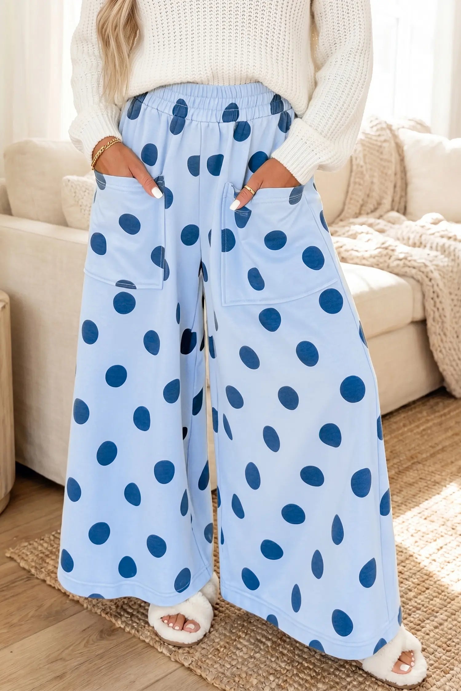 A person wearing light blue wide-leg pajama pants with dark blue polka dots, standing in a living room setting.