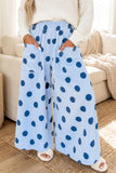 A person wearing light blue wide-leg pajama pants with dark blue polka dots, standing in a living room setting.