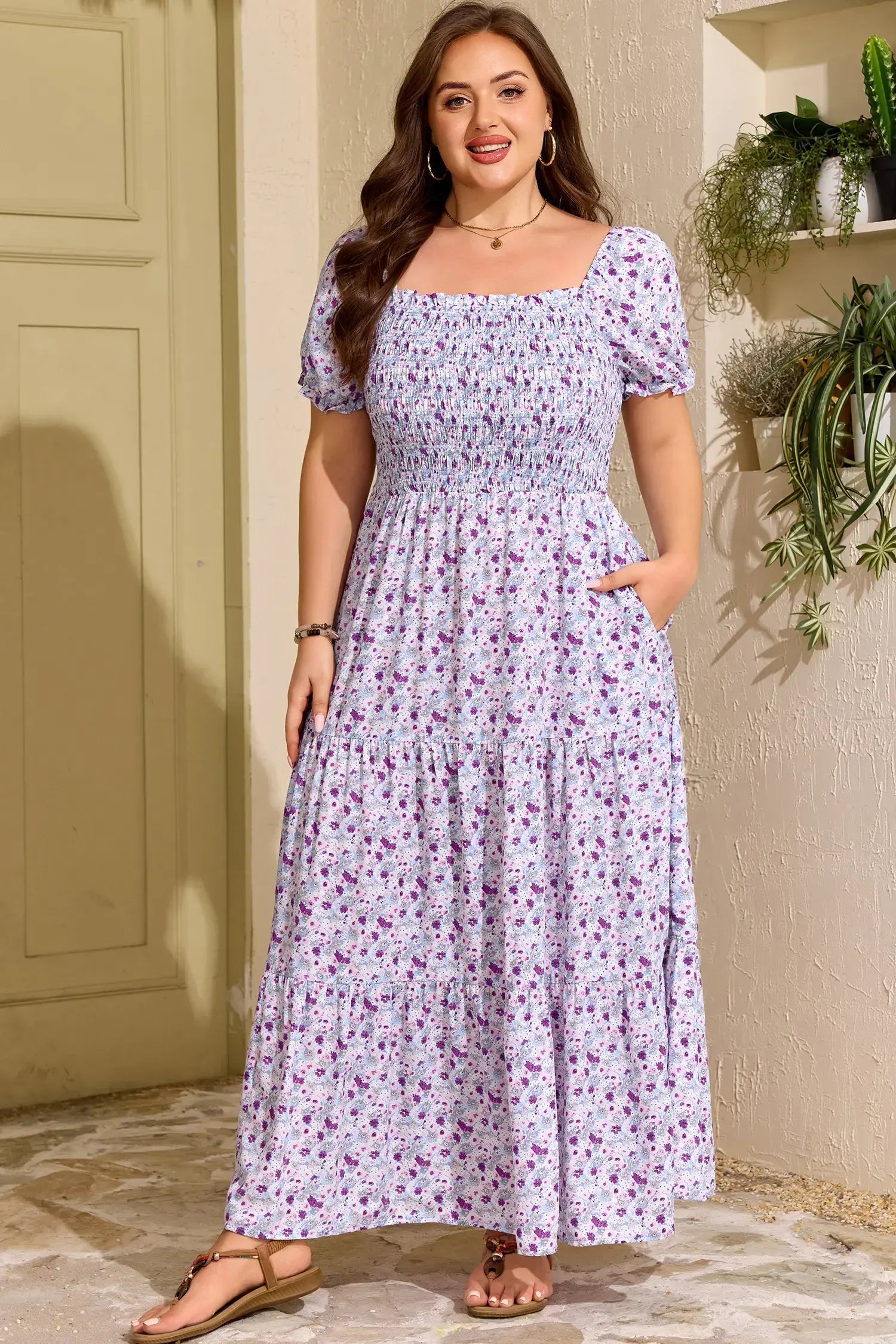 Woman wearing a floral dress standing in a sunlit room with plants.