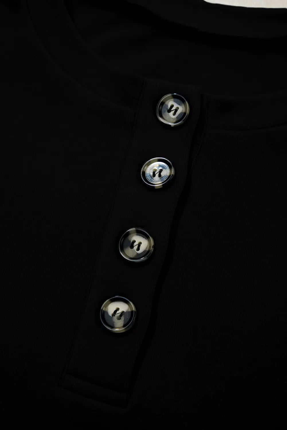 Close-up of a black Henley-style top with four metallic buttons down the center chest.