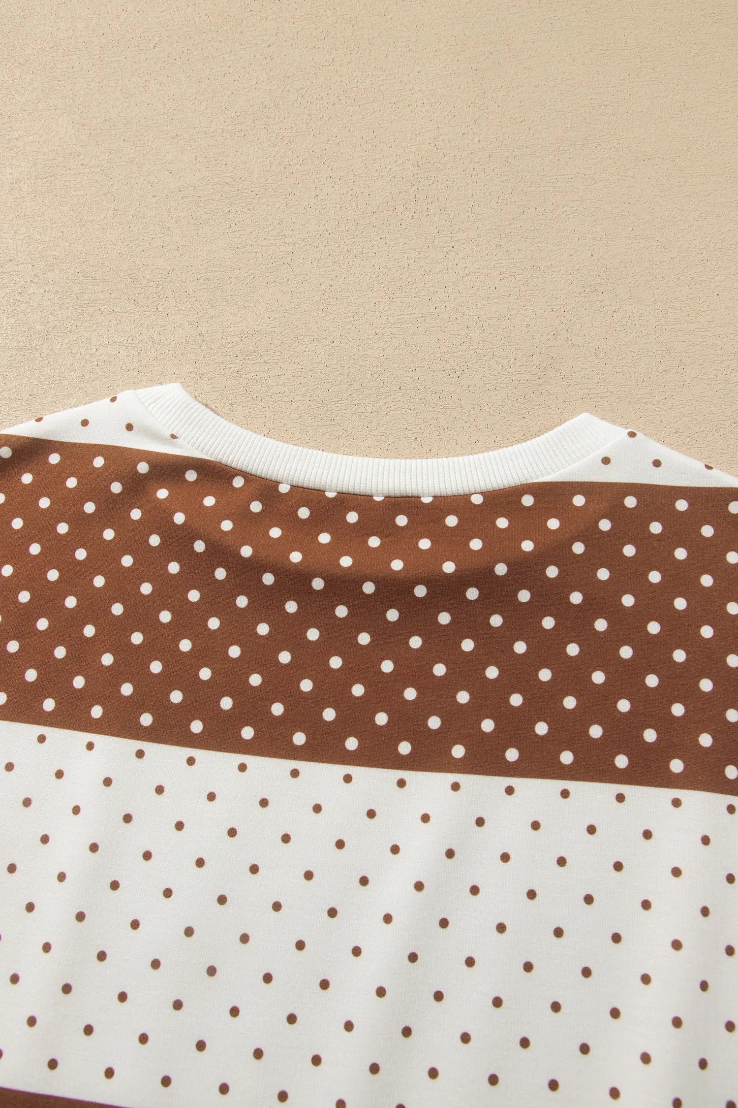 Close-up of a color-blocked sweatshirt with brown and white polka dot panels.