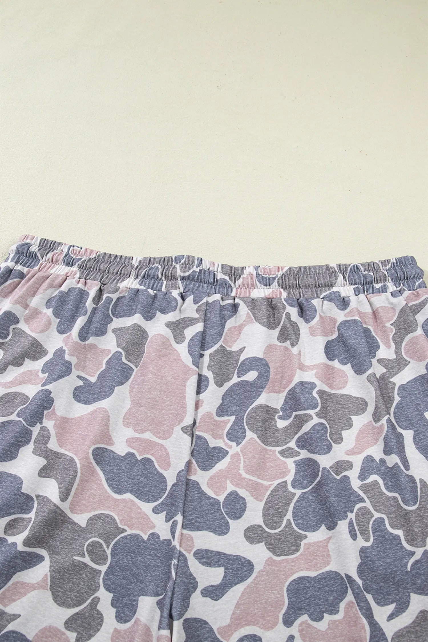 Close-up of a pair of shorts with an elastic waistband, featuring a pink, gray, and white abstract camouflage pattern.