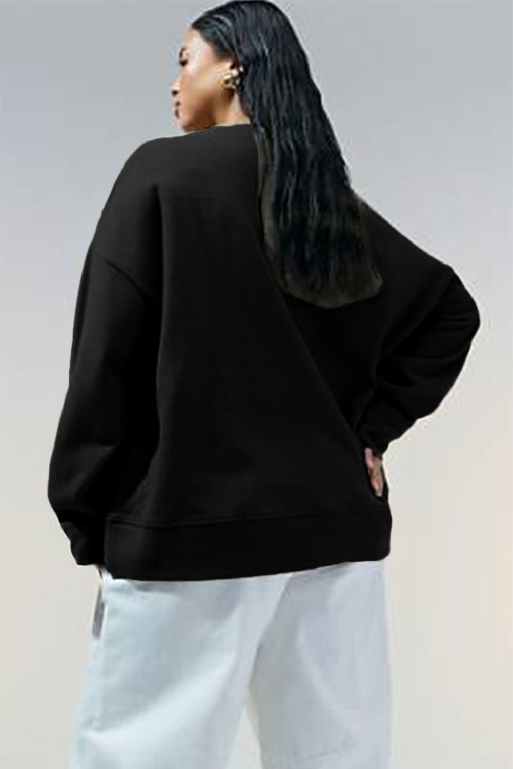 Woman shown from behind wearing a black oversized sweatshirt with white pants.