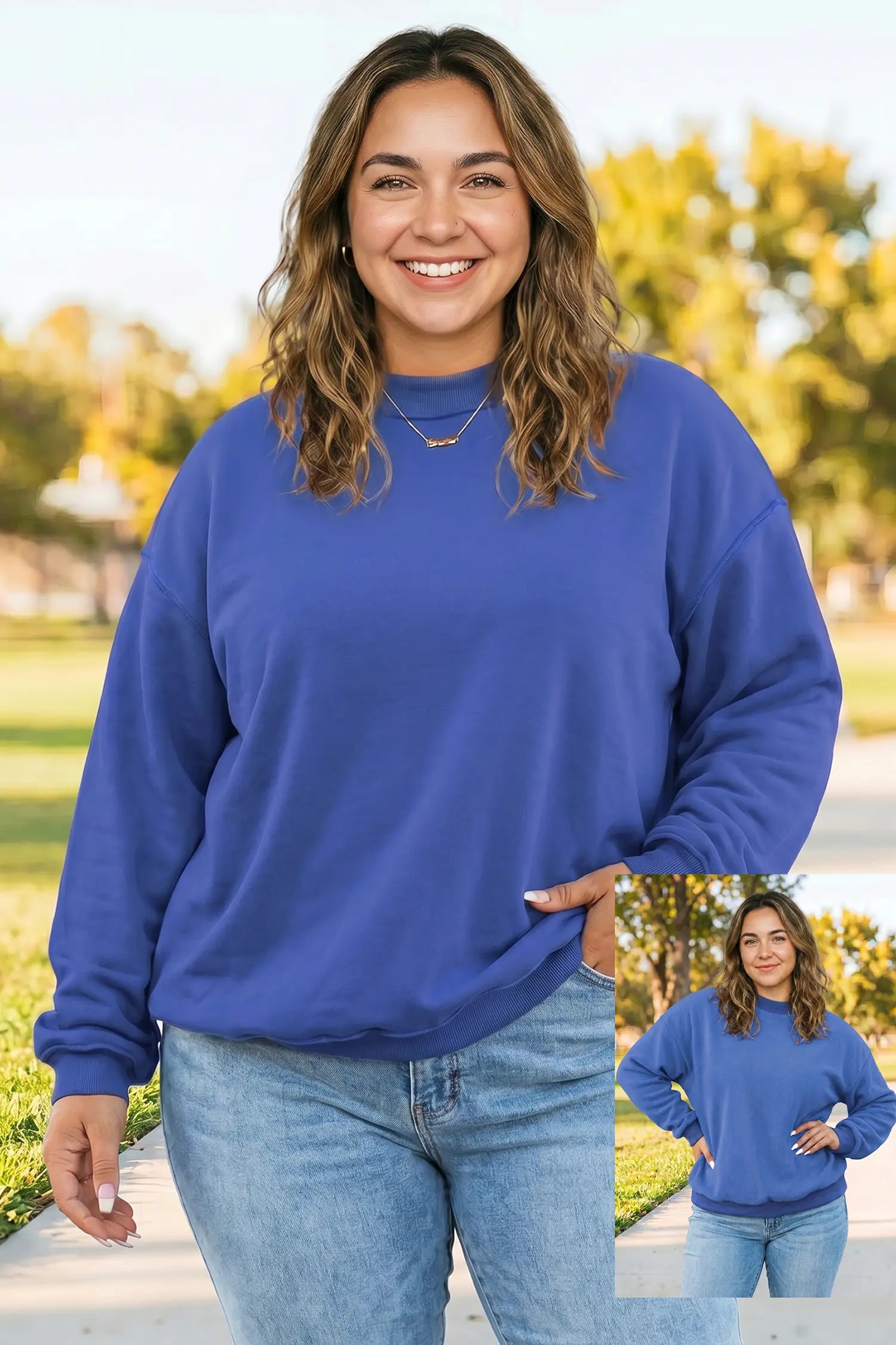 A woman wearing a royal blue crewneck sweatshirt and light wash jeans, standing outdoors on a paved path with trees in the background. A small inset image in the bottom right corner shows a front view of the sweatshirt.