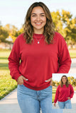 A woman wearing a red crewneck sweatshirt and light blue jeans, standing outdoors on a paved path with trees in the background. A smaller inset image in the bottom right corner shows the same person wearing the sweatshirt.