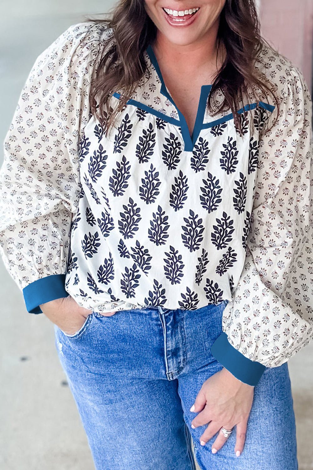 Woman wearing a floral blouse with blue accents and jeans, standing against a neutral background.