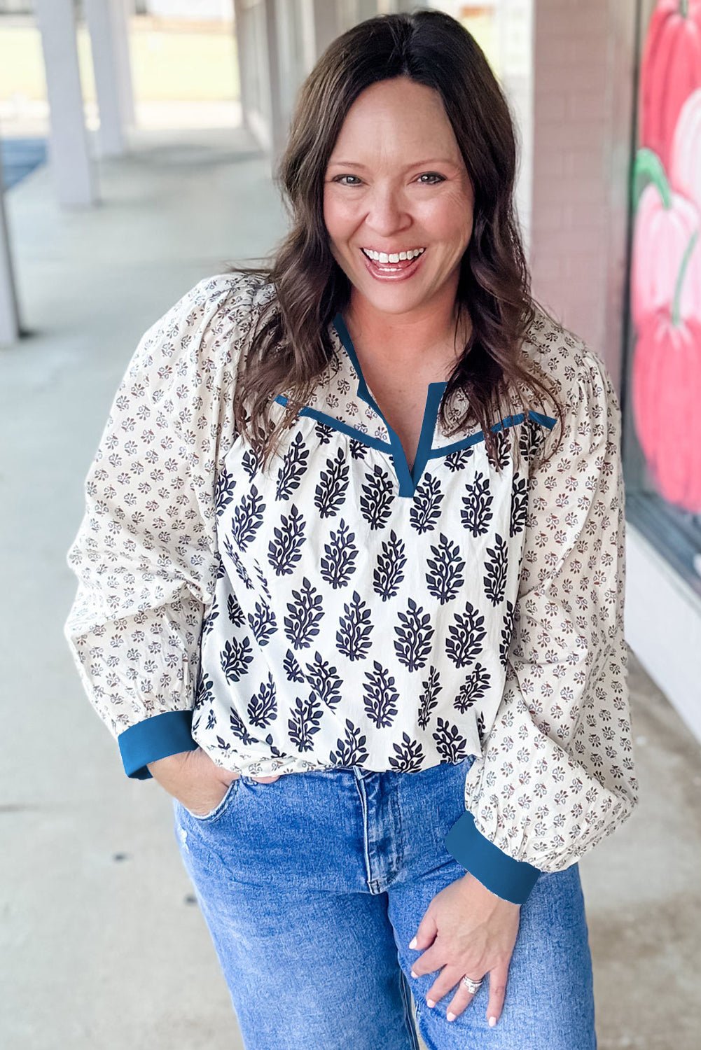 Woman wearing a patterned blouse and blue jeans standing in an outdoor setting.