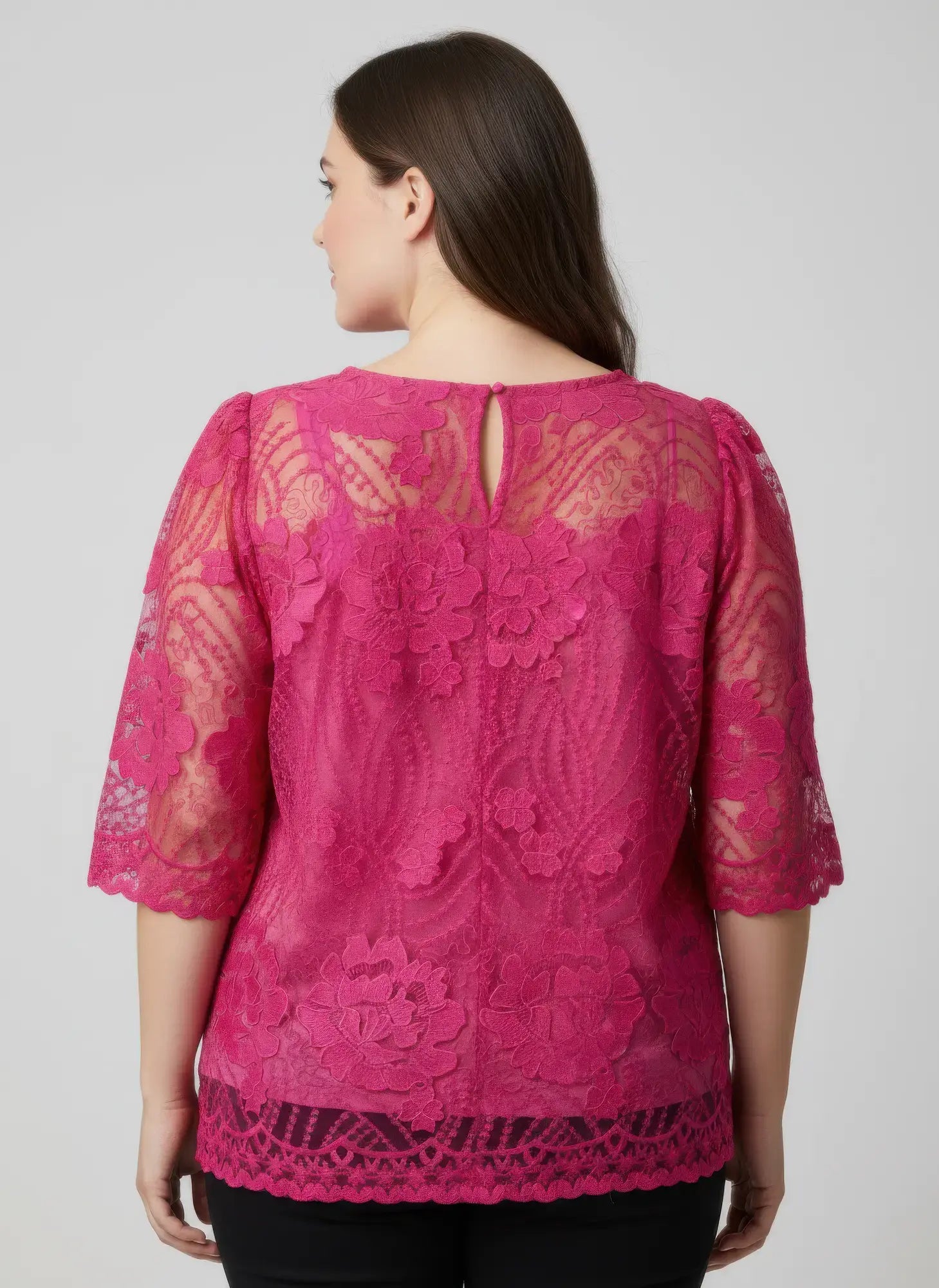 Woman wearing a pink lace top against a plain background