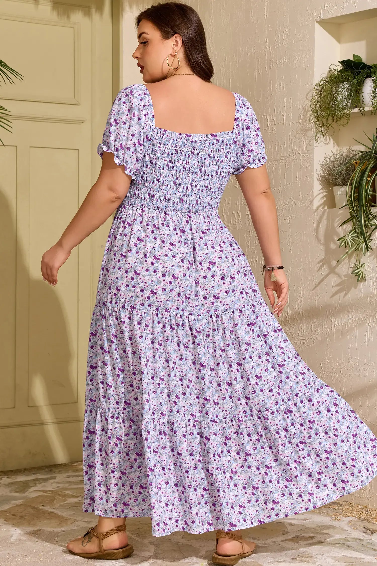 Woman wearing a floral dress standing in a sunlit room with plants.
