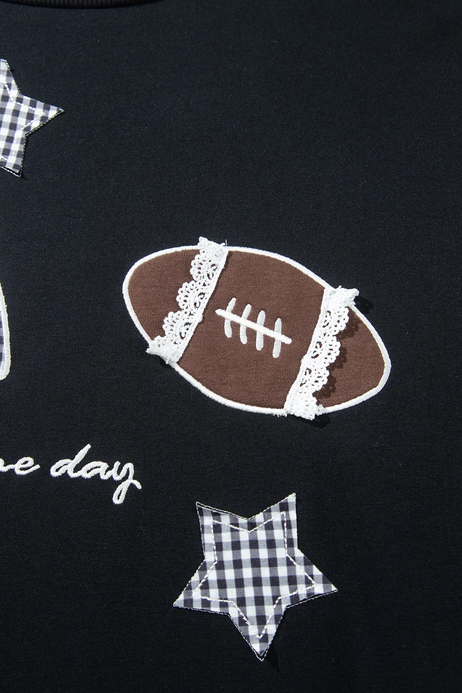 Close-up of a black garment with football, gingham star patches, and white script text.