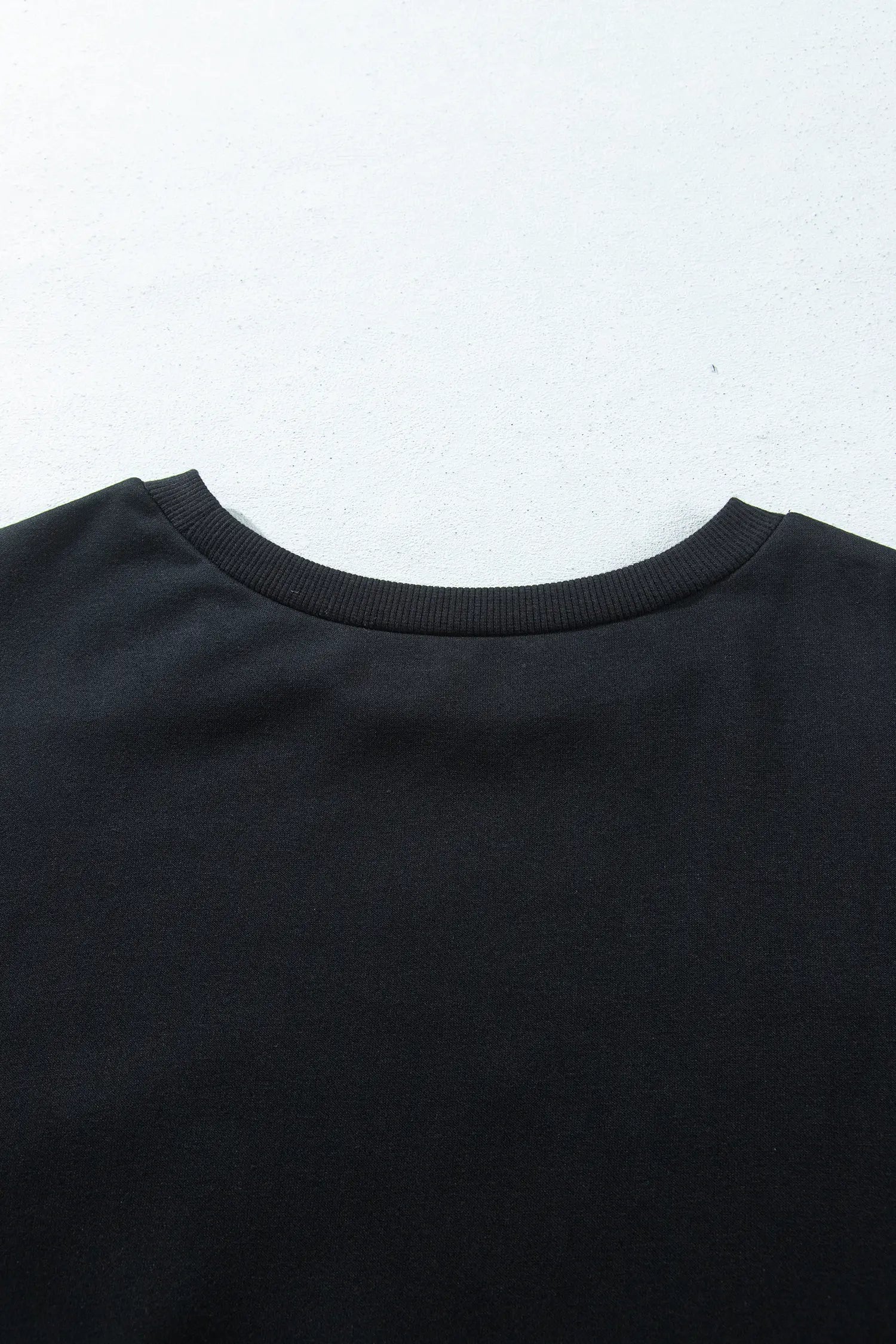 Close-up of the back neckline of a black crewneck t-shirt against a plain white background.