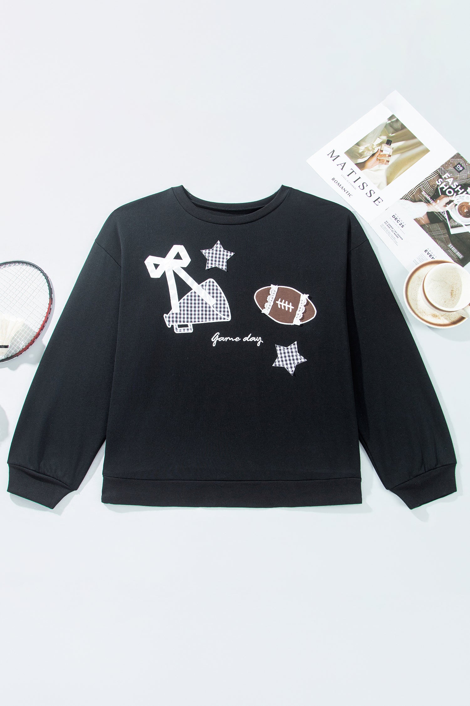 Black sweatshirt with white bow, football, and star graphics, styled flat with a tennis racket.