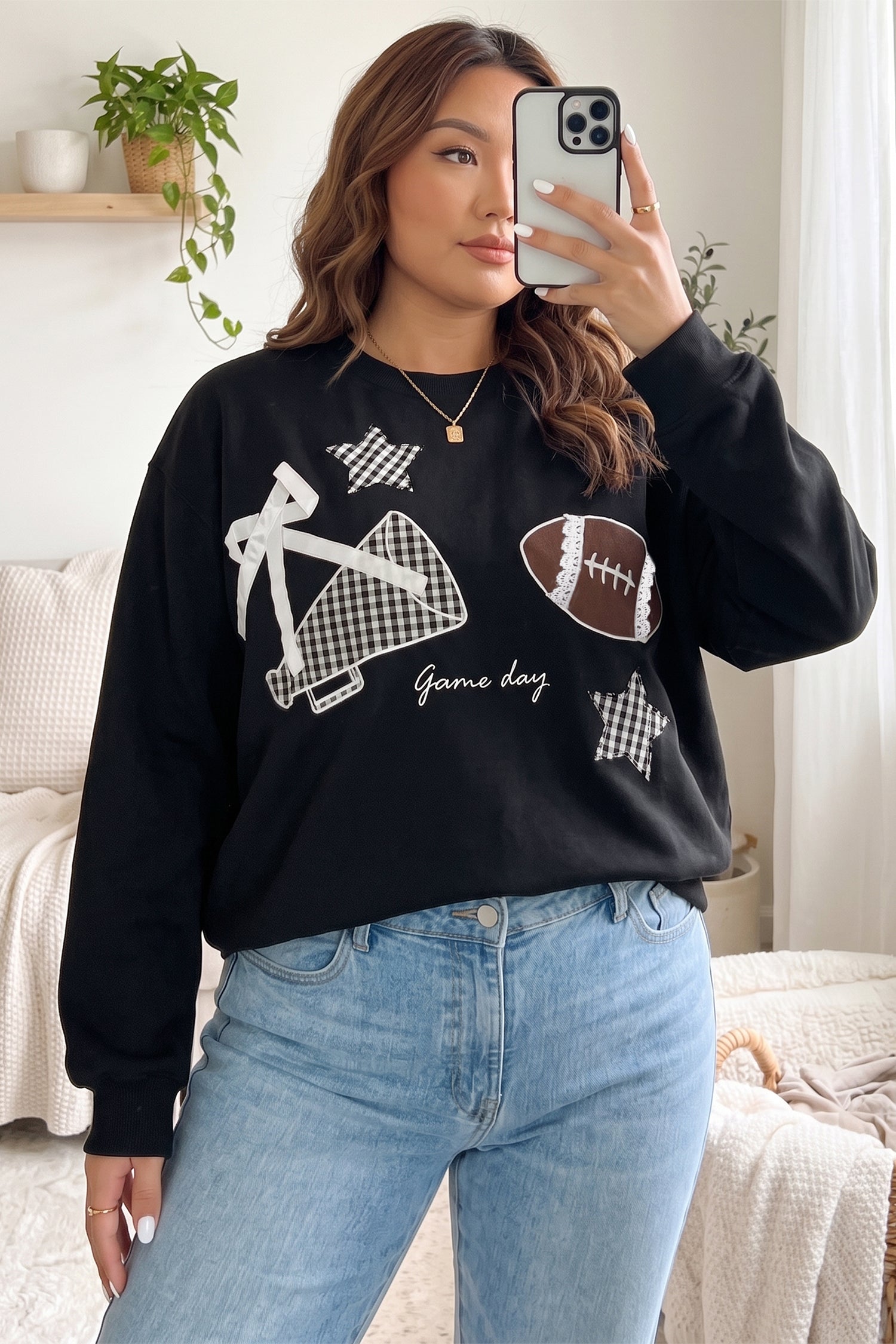 Woman taking a mirror selfie in a black “Game Day” football sweatshirt with light blue jeans.