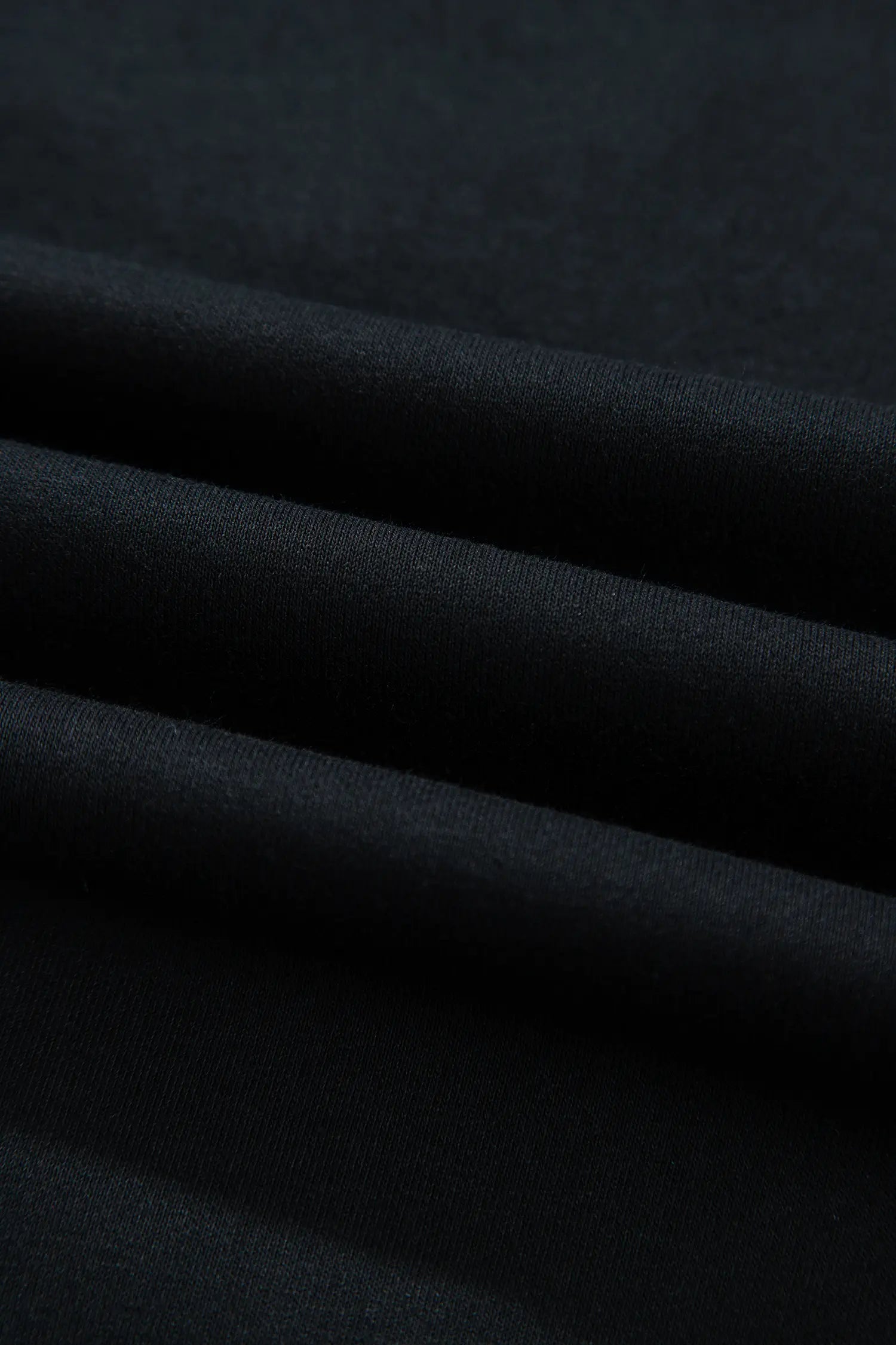 A close-up of draped black fabric with soft folds showing its texture and matte finish.
