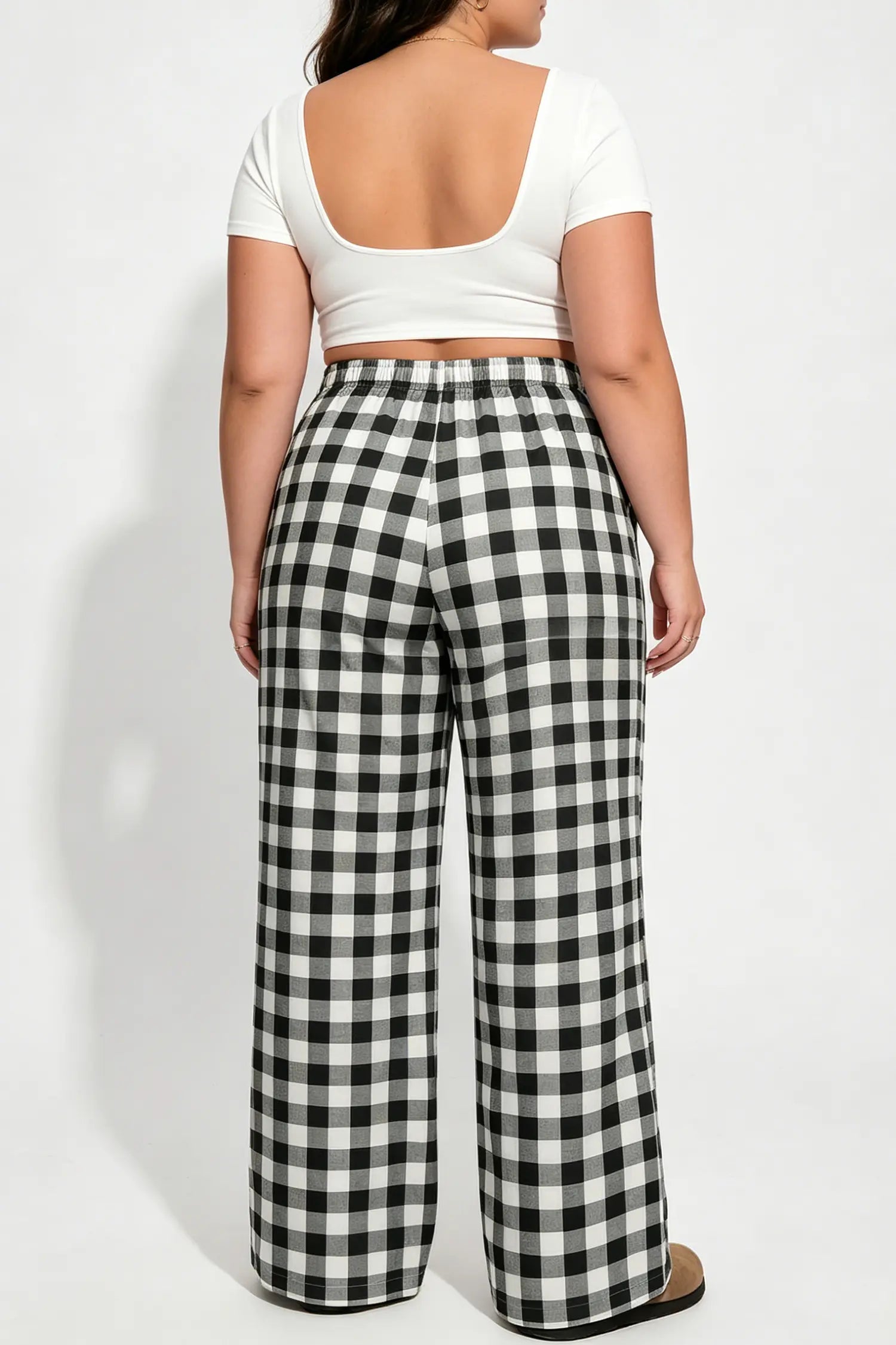 Person wearing a white top and black and white checkered pants on a white background