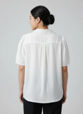 Person wearing a white blouse with a plain background