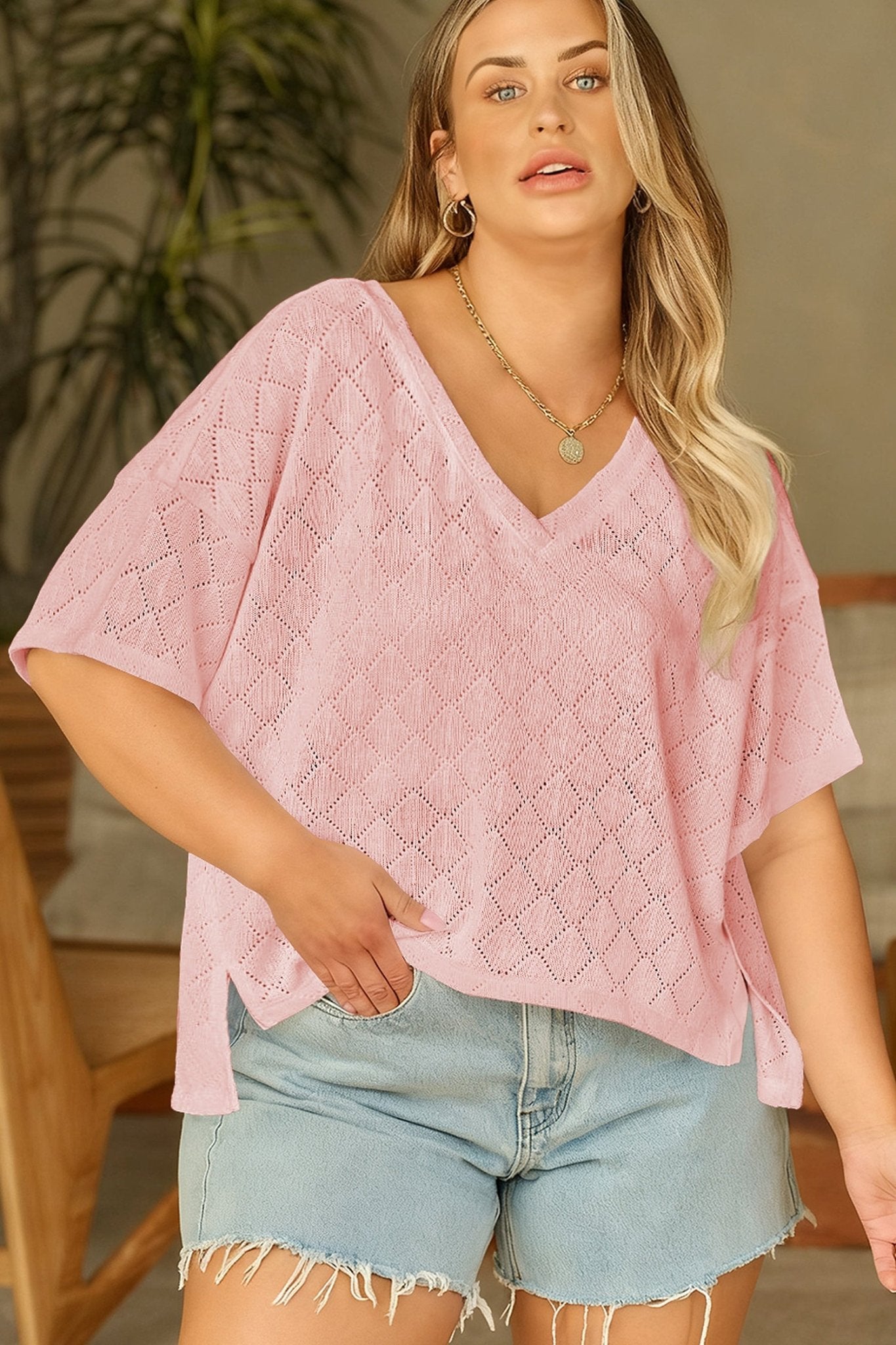 Woman wearing a pink textured top and denim shorts indoors.