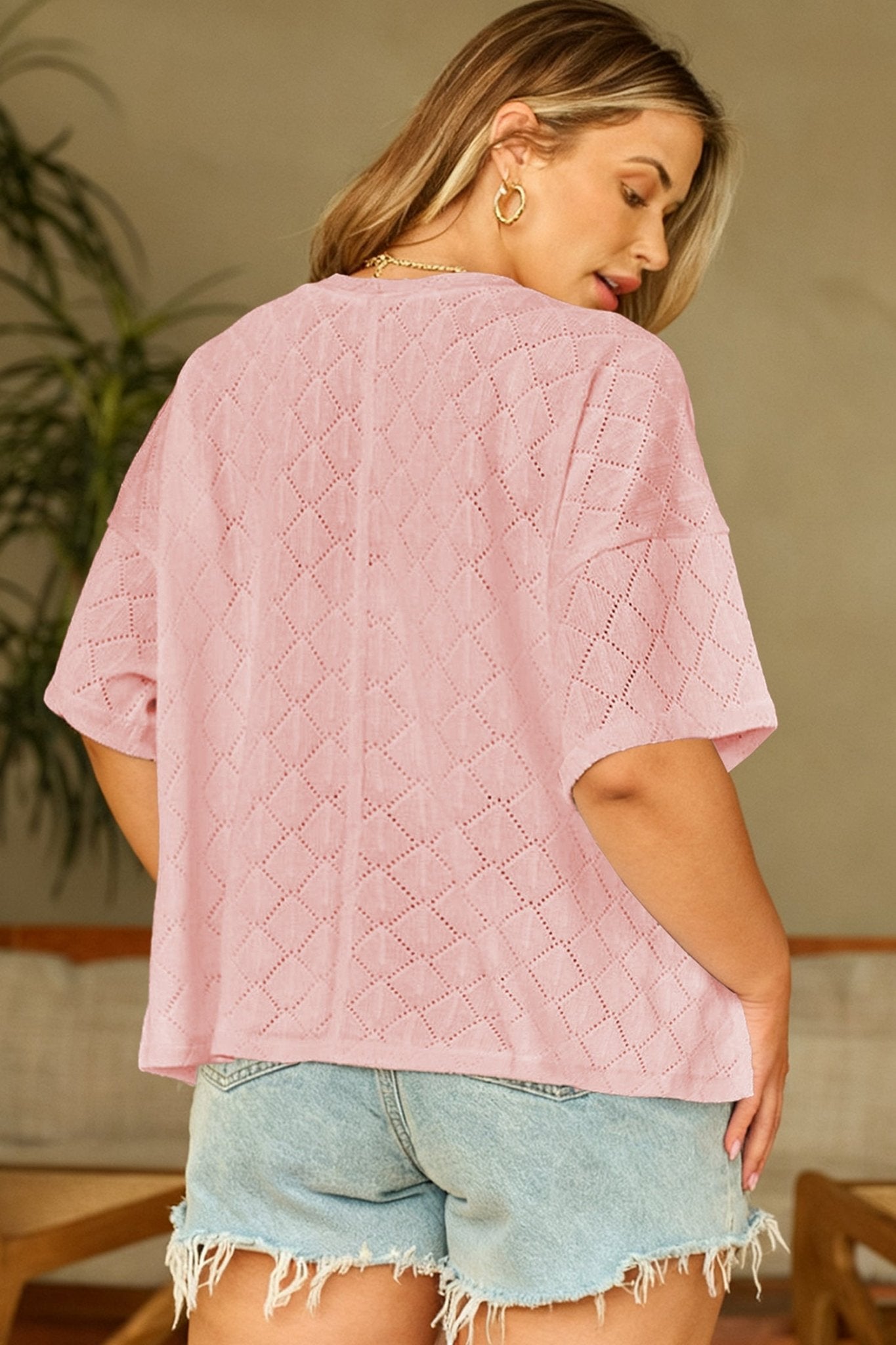 Woman wearing a pink textured top and denim shorts indoors.