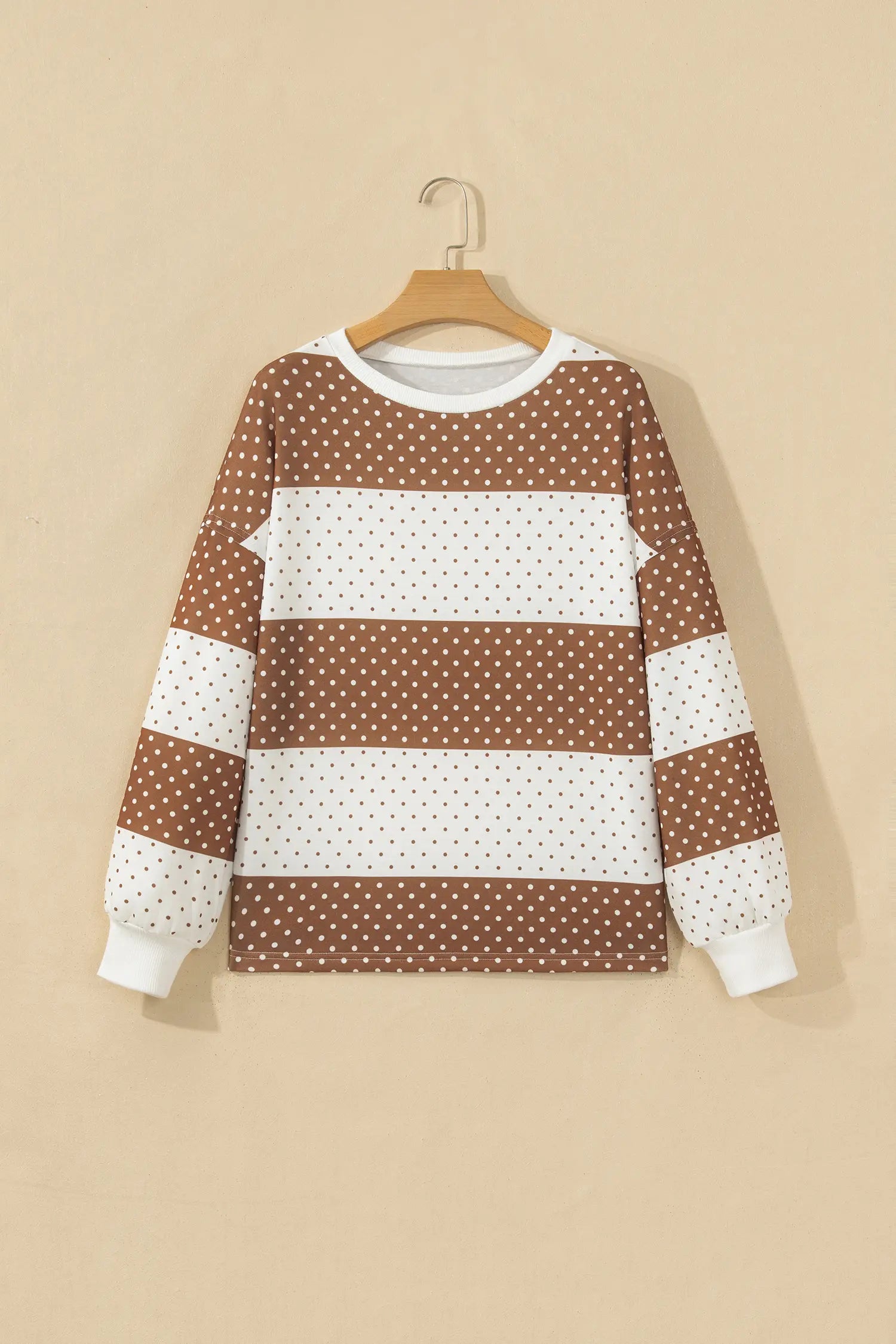 Brown and white striped long-sleeve crewneck sweatshirt with polka dots on a hanger.