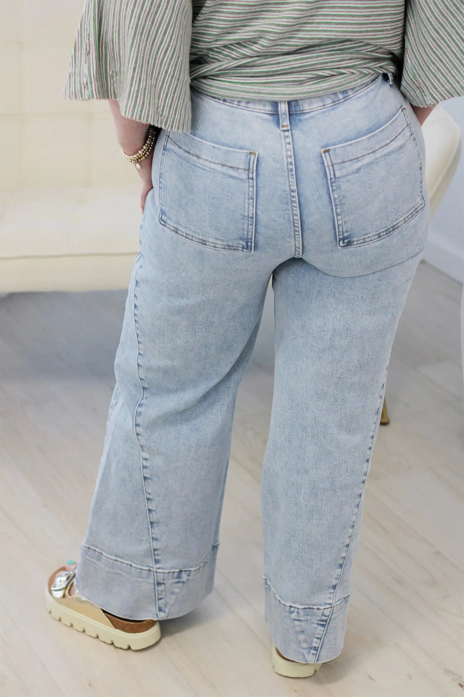 A person shown from the back wearing light-wash wide-leg jeans, a striped top, and beige platform sandals in an indoor setting.