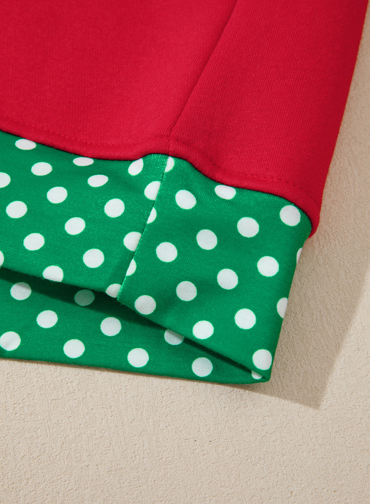 A close-up of a folded garment showing two contrasting fabric panels: a solid bright red upper section and a green lower section with white polka dots.