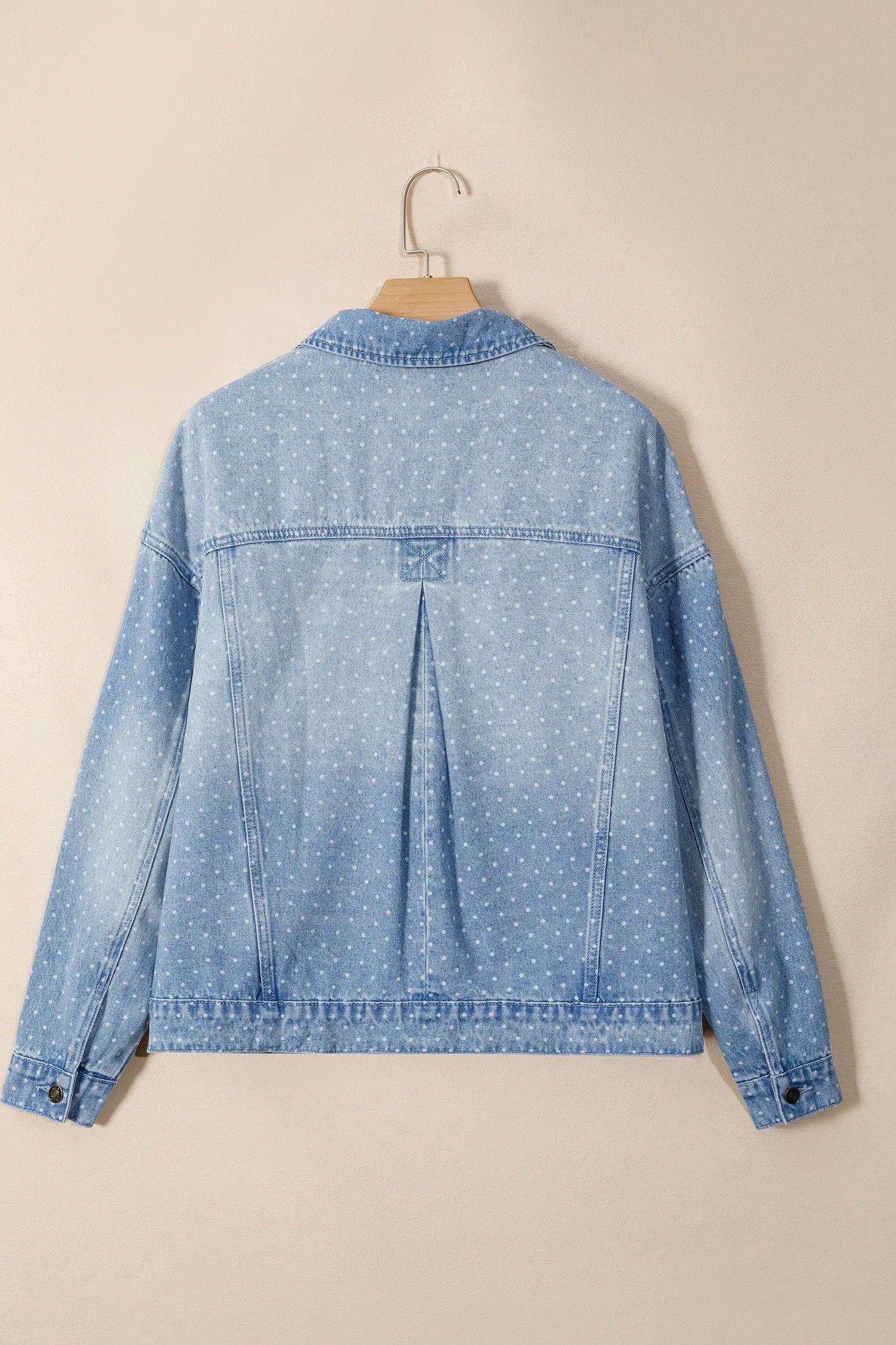 Light blue denim jacket with white polka dots, back view, hanging on a wooden hanger.