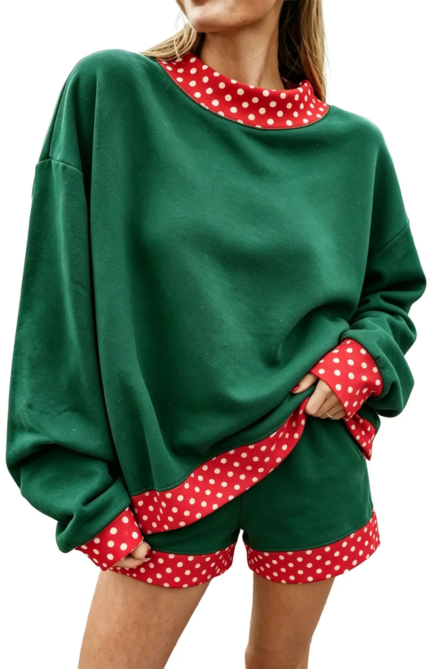 A woman wearing a green oversized sweatshirt and matching shorts with red and white polka dot trim details, shown against a plain white background.