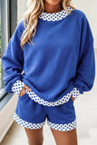 A woman wearing a matching royal blue lounge set with white and blue polka dot trim details on the crewneck, cuffs, hem, and shorts.