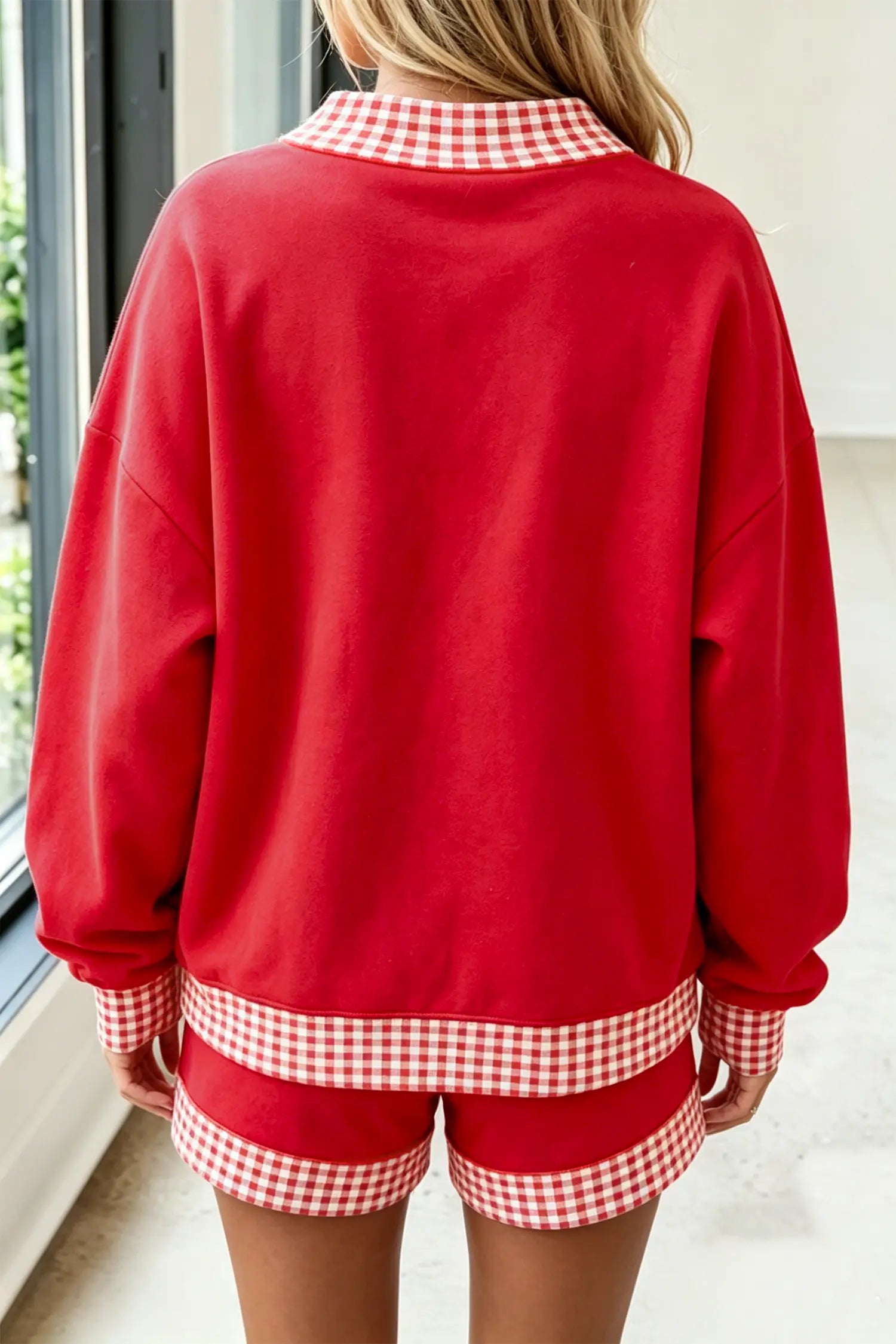 A person shown from the back wearing a red sweatshirt and matching shorts with red-and-white gingham trim on the collar, cuffs, and hem.