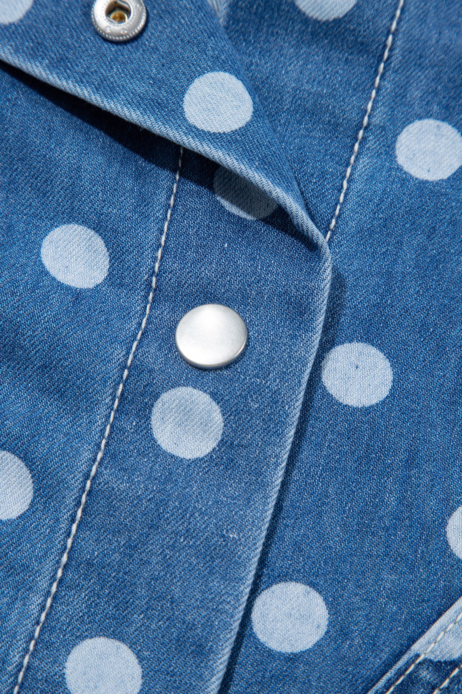 Close-up of a blue denim shirt with white polka dots and silver snap buttons.