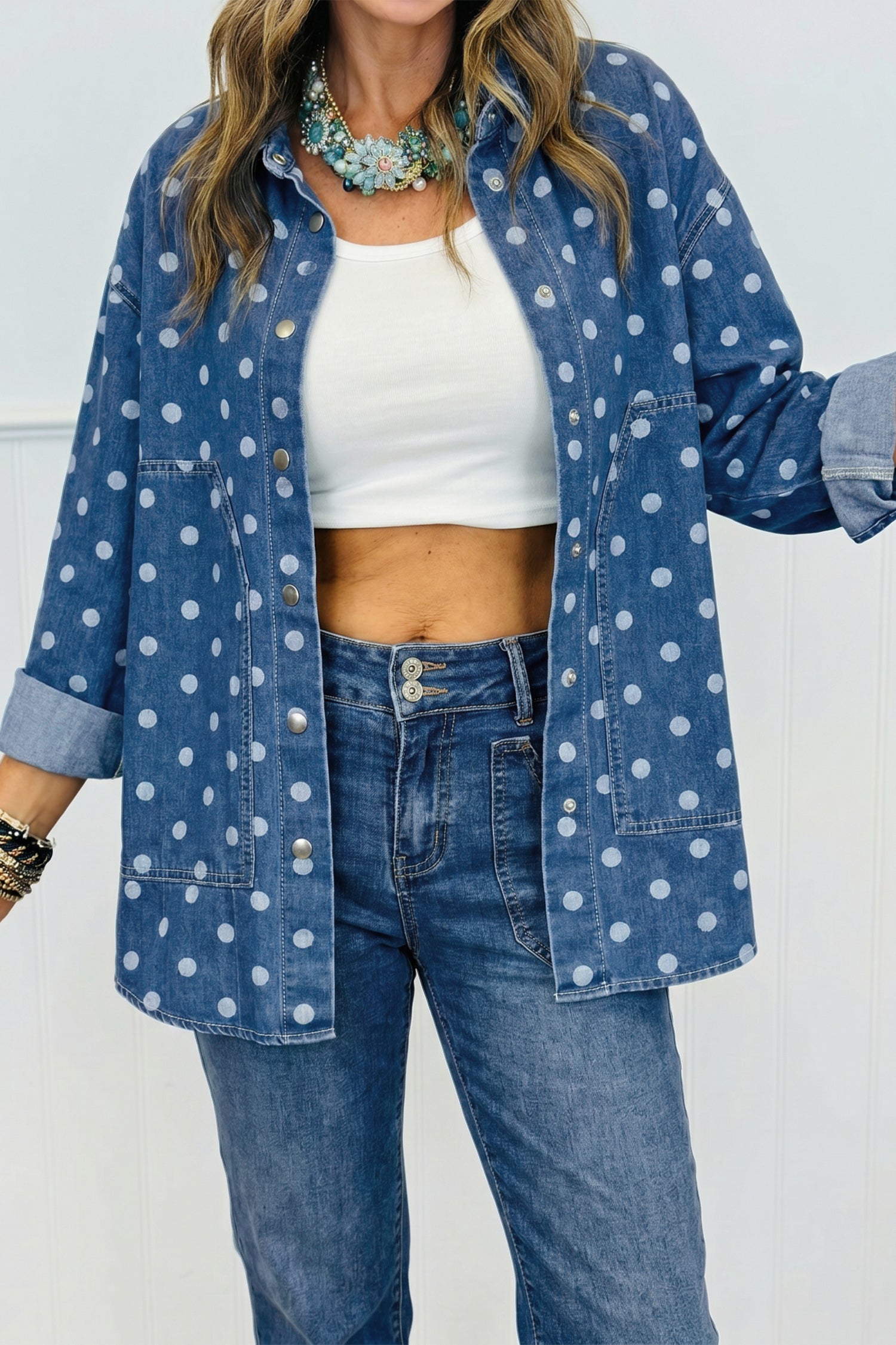 Woman wearing oversized blue denim shirt with white polka dots over white crop top and blue jeans.