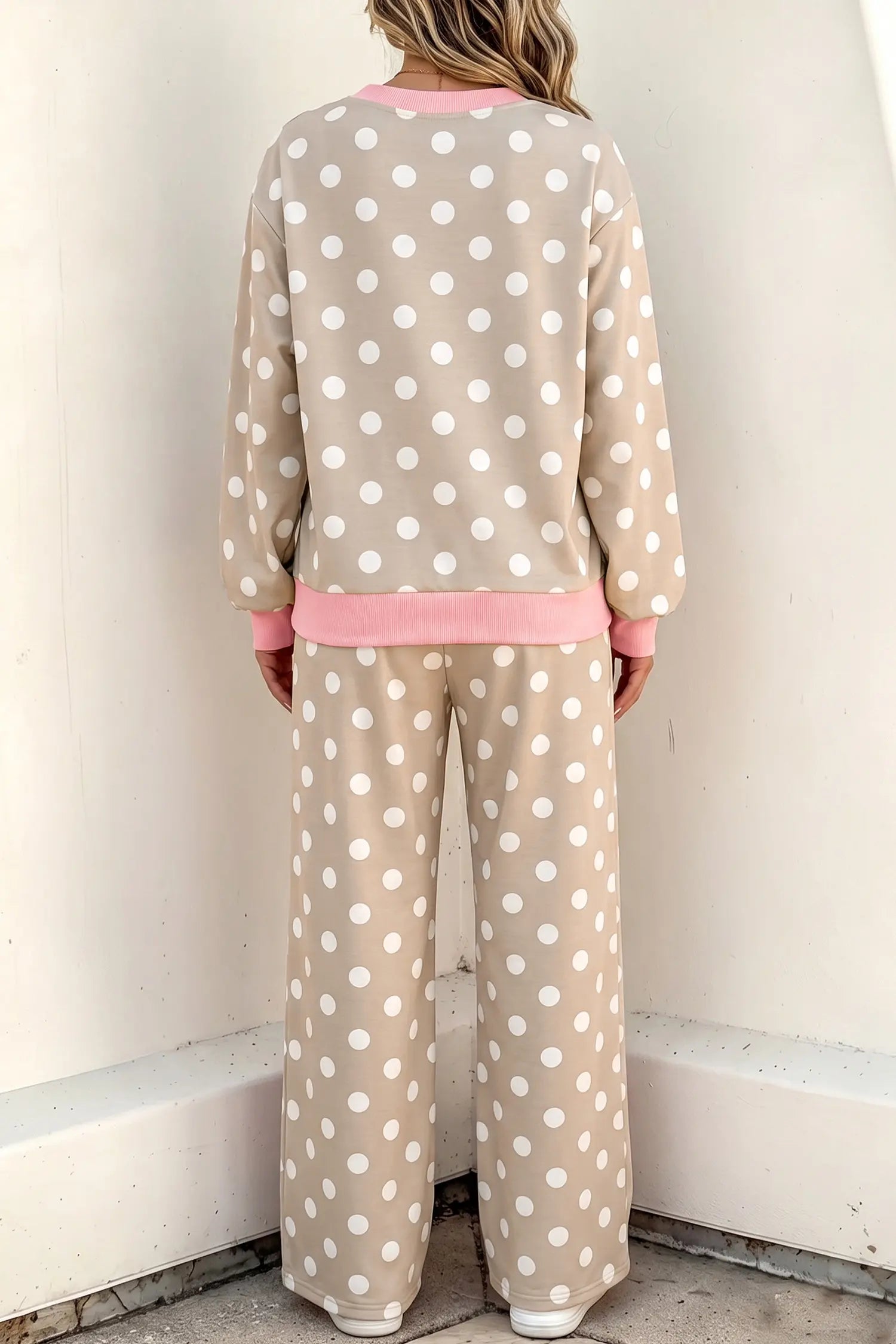 A person shown from the back wearing a beige and white polka dot lounge set with pink trim, standing against a plain off-white wall.