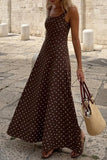 Woman wearing a brown polka dot dress holding a beige bag on a stone pavement.