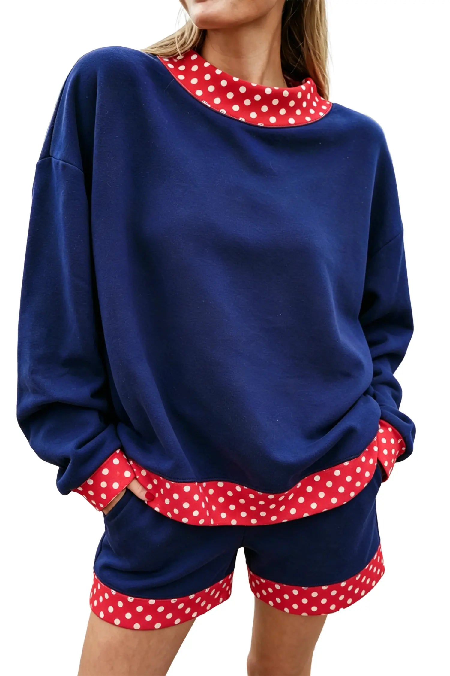 A woman wearing a navy blue lounge set with red and white polka dot trim, including a long-sleeve sweatshirt and matching shorts, shown against a plain white background.