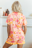 A woman viewed from behind wearing a short-sleeve ruffled romper with a pink, orange, and yellow pumpkin pattern on a light peach background, posed in front of a white fireplace mantel.