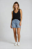 Woman wearing a black tank top with embellishments and denim shorts on a white background