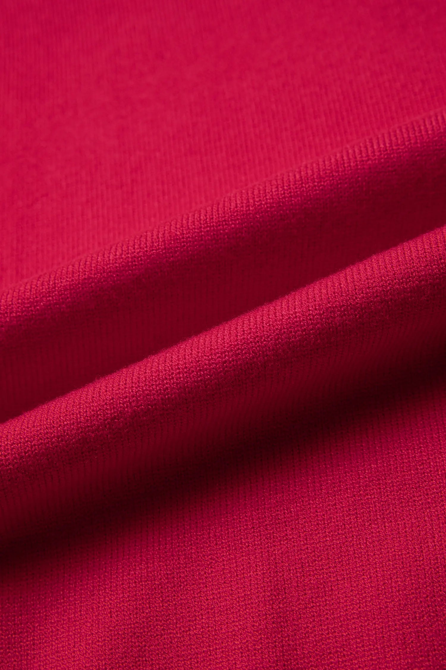A close-up of bright pink knit fabric with soft diagonal folds showing the texture and color.