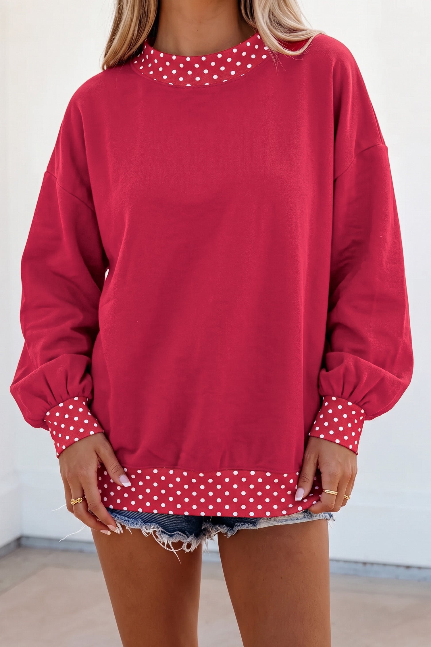 Woman in red sweatshirt with white polka-dot trim and denim shorts.
