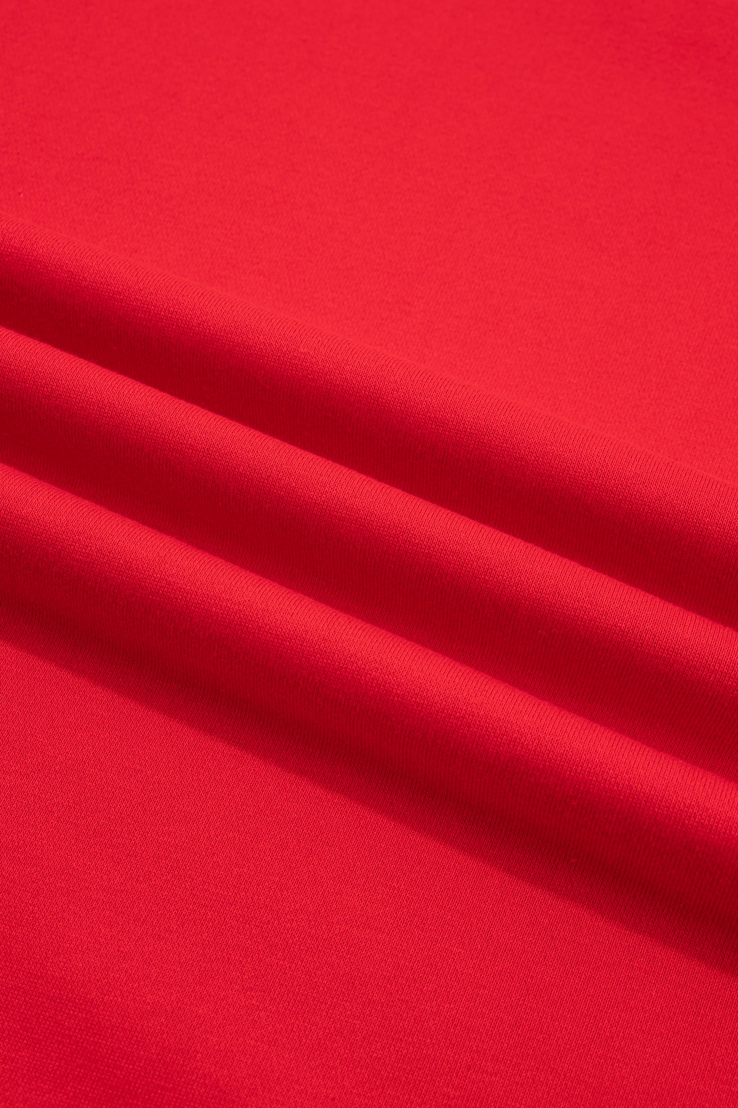 A close-up of bright red fabric with soft diagonal folds and a smooth texture.
