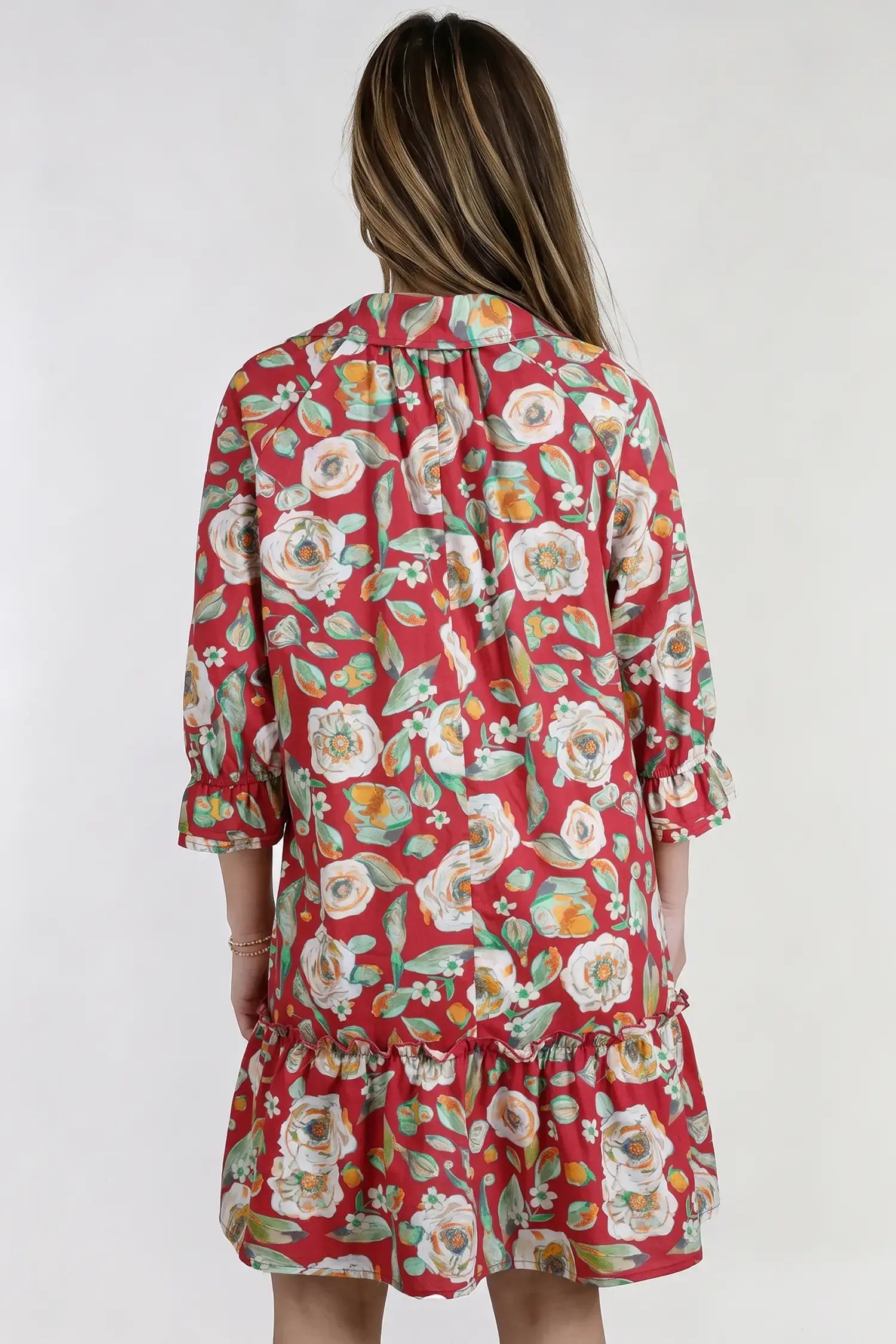 A woman viewed from the back wearing a red floral shirt dress with three-quarter sleeves and a ruffled hem, set against a plain light gray background.