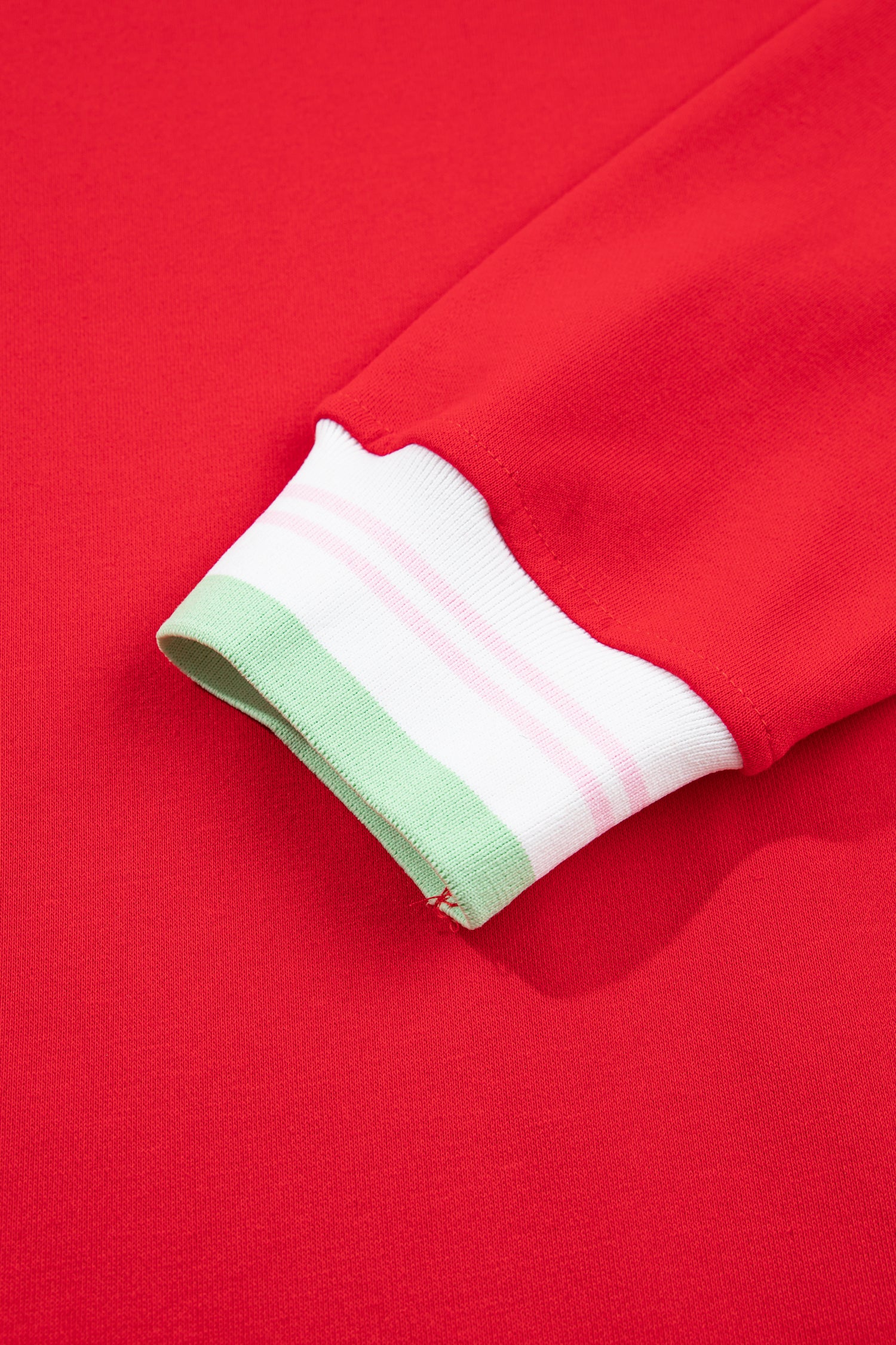 Close-up of a red sweatshirt sleeve cuff with a white ribbed band featuring light pink stripes