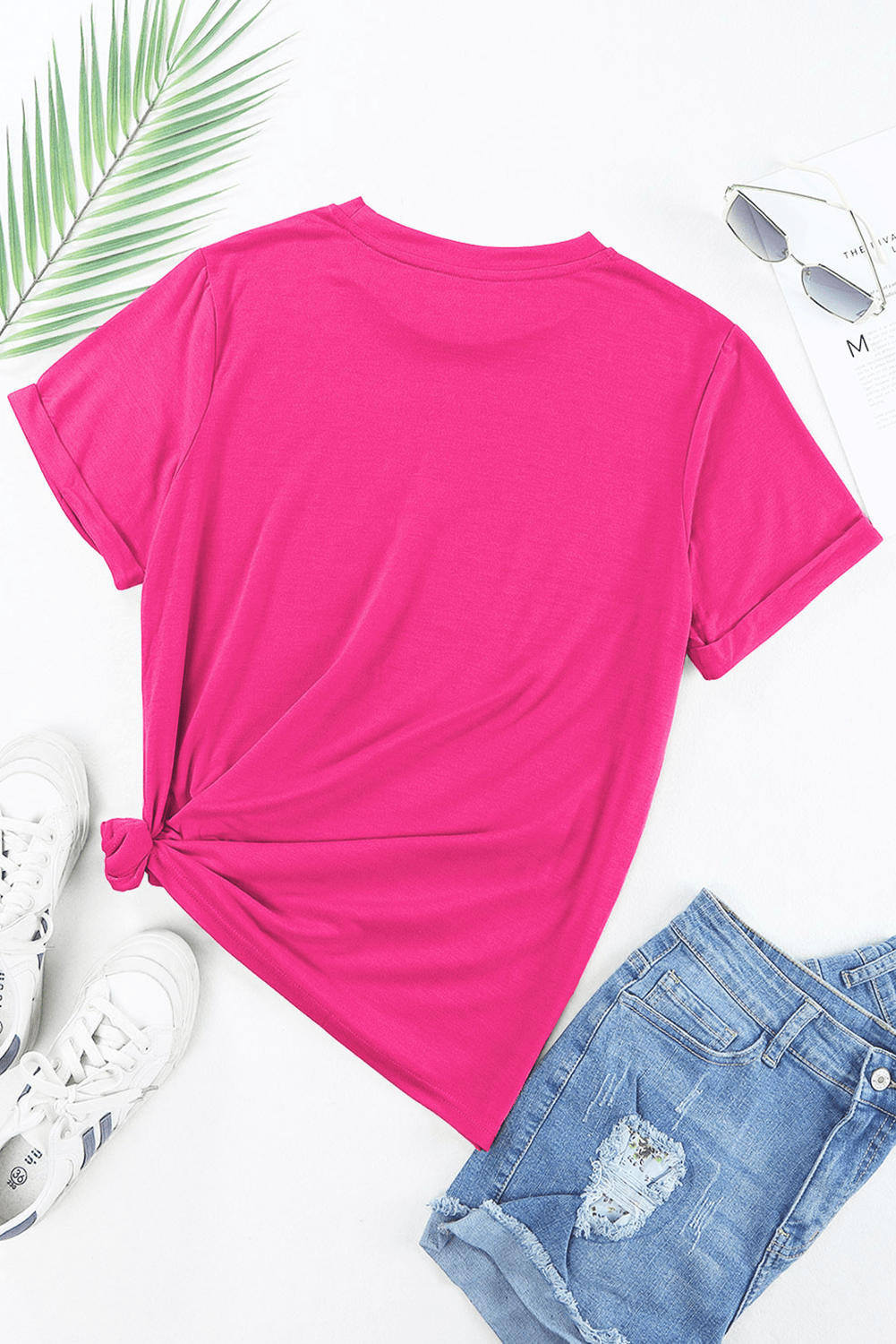 Pink t-shirt with a knot detail, white sneakers, and denim shorts on a white background.