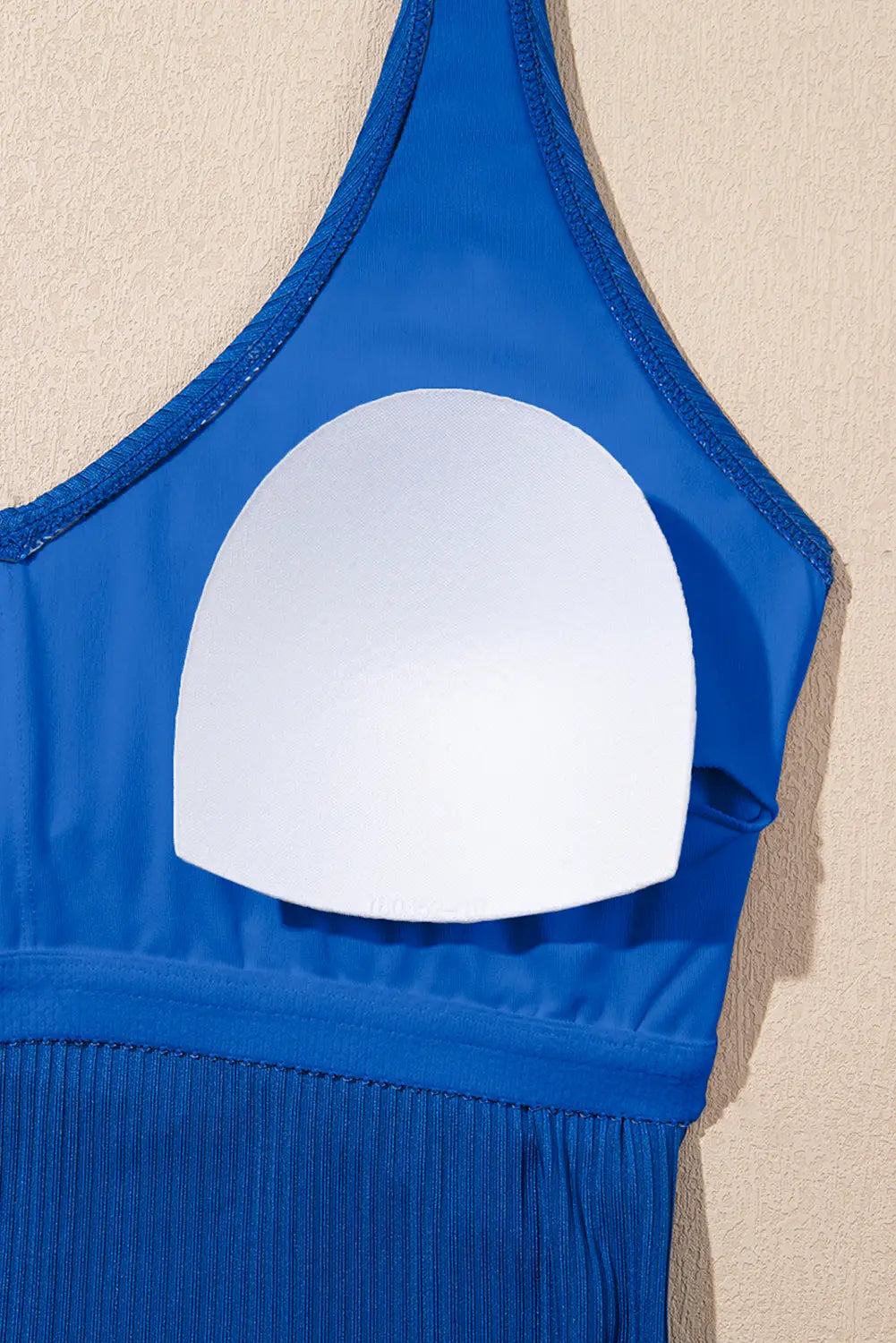 Blue swimsuit top with a white circular cutout on a beige background